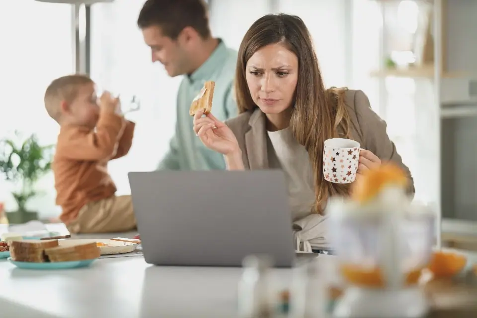Parents and a toddler at the kitchen table with a laptop open during breakfast