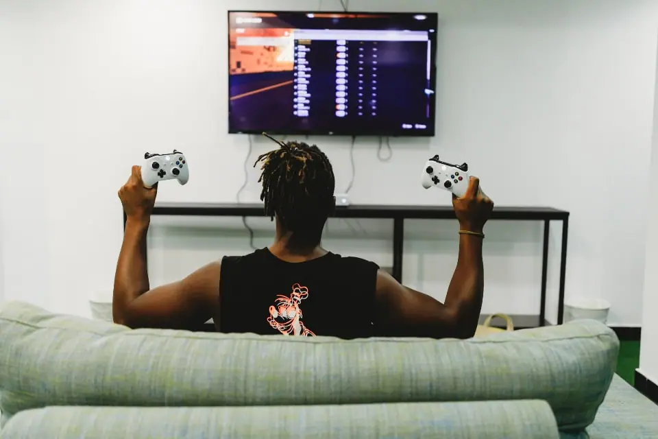 A person on a sofa playing a console game on a large wall-mounted TV