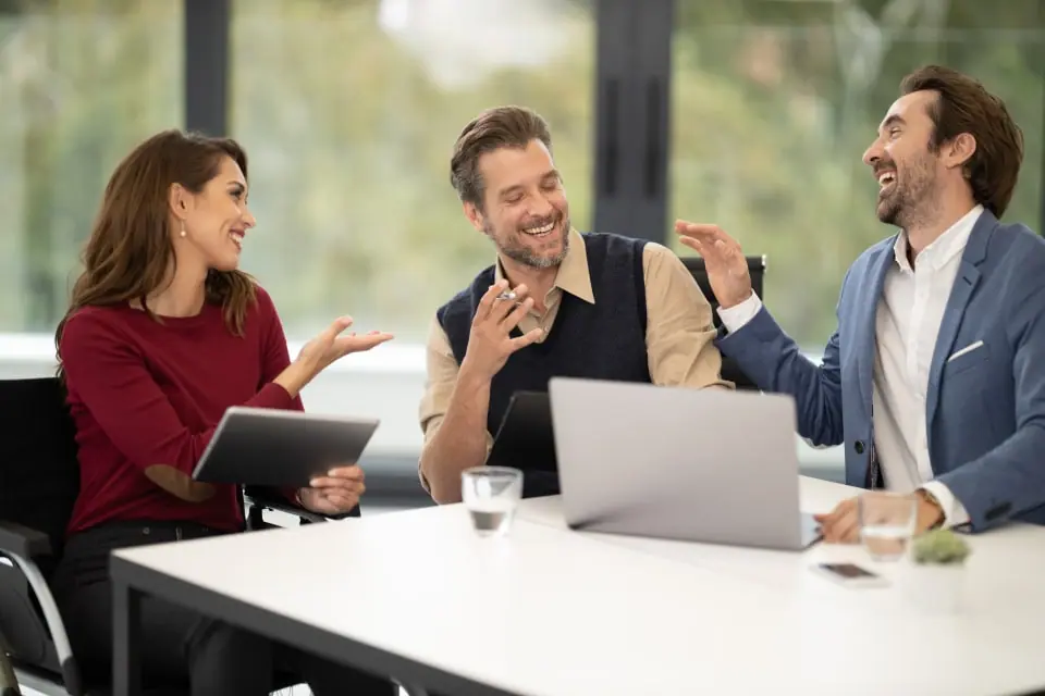 Friendly specialists laughing together while going over options on a laptop and tablet